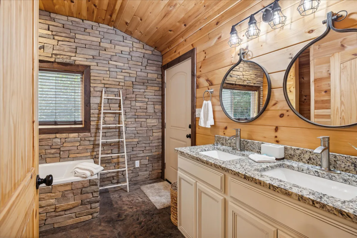 A cozy bathroom featuring a double sink vanity with round mirrors, a rustic stone wall, and warm wooden finishes. The space is inviting and practical, providing both privacy and luxury for guests.