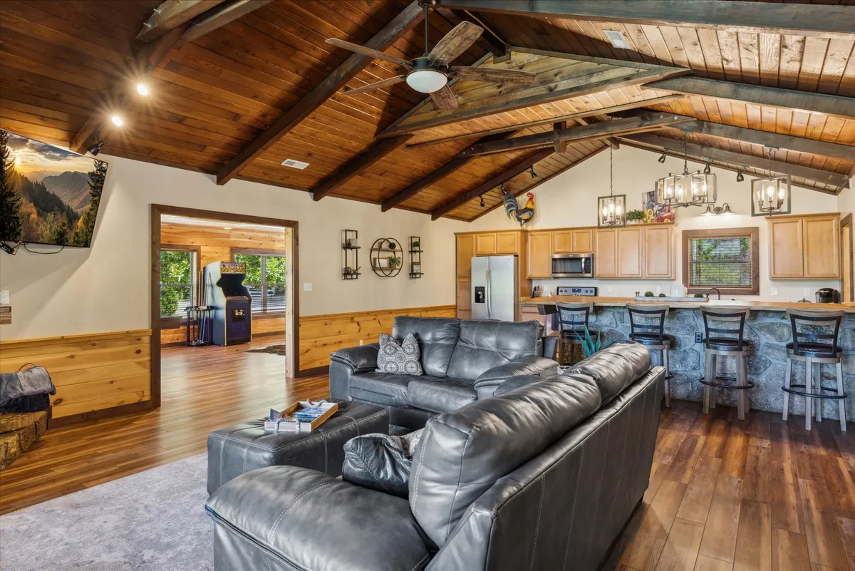 This interior shot showcases the open-concept living area connected to the kitchen, with a large leather sofa, kitchen island with bar stools, and wooden ceiling beams. The entertainment center and TV are visible, suggesting a space where meals and relaxation seamlessly blend. The dining and lounge zones are clearly defined yet interconnected, fostering togetherness during meals and gatherings.