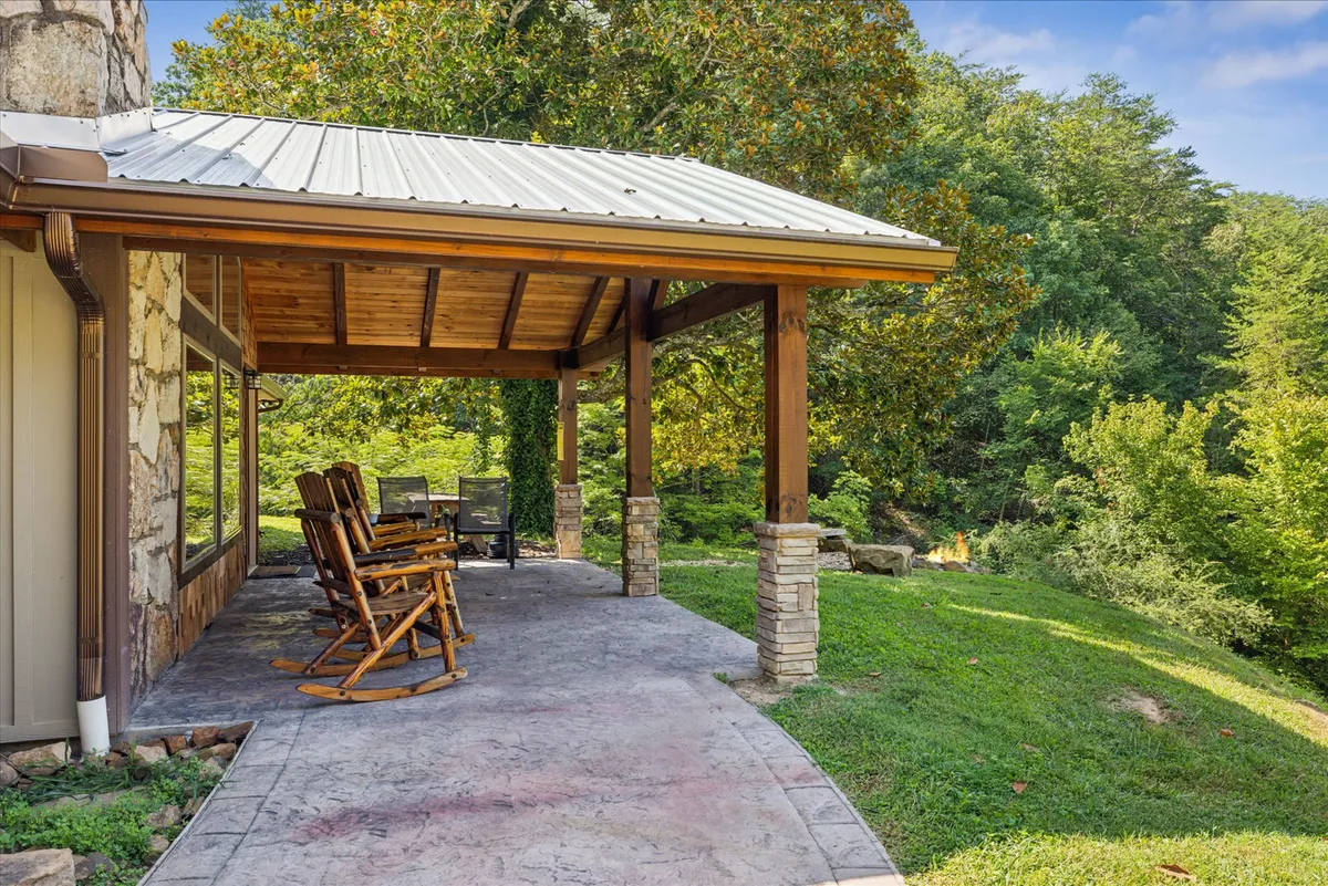This cozy exterior shot features a porch with classic rocking chairs and sturdy stone pillars, framed by wooden beams. The setting is perfect for relaxing with a morning coffee or sharing an intimate moment while gazing at the serene natural surroundings.