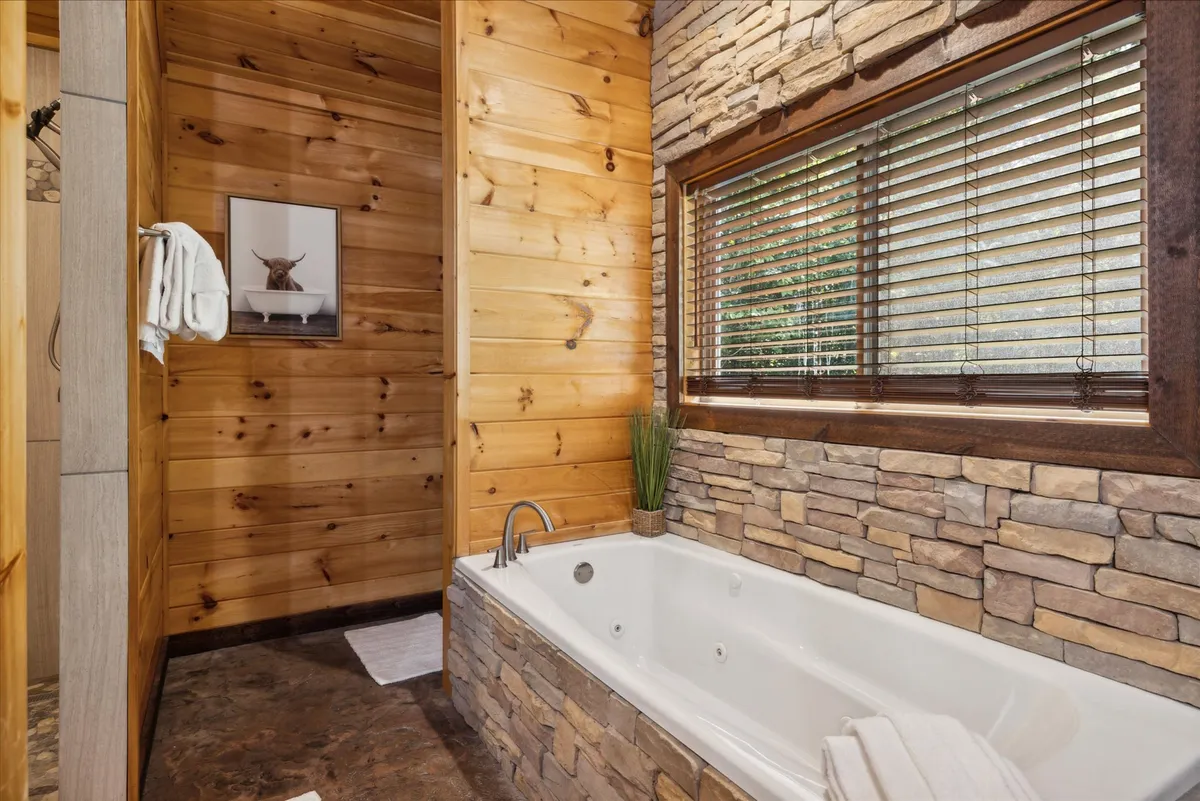 A tranquil bathroom with a bathtub set against a stone wall, wood paneling, and a window with blinds. The spa-like environment invites relaxation and unwinding after a day of adventure.